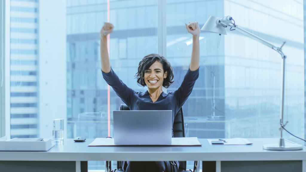 Shot of the Beautiful Businesswoman Sitting at Her Office Desk, Raising Her Arms in a Celebration of a Successful Job Promotion.